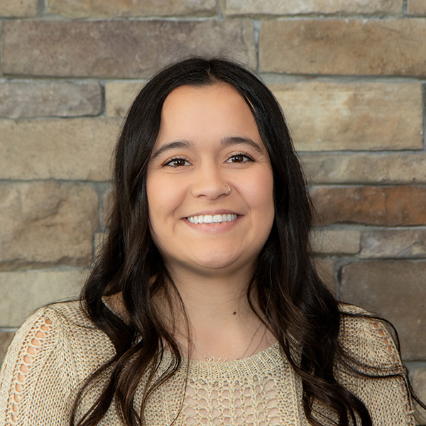 Sydney McCall, Resident Services Director at The Barrymore Senior Living, smiling in a professional headshot. She wears a light tan knit top, with a neutral stone wall background.