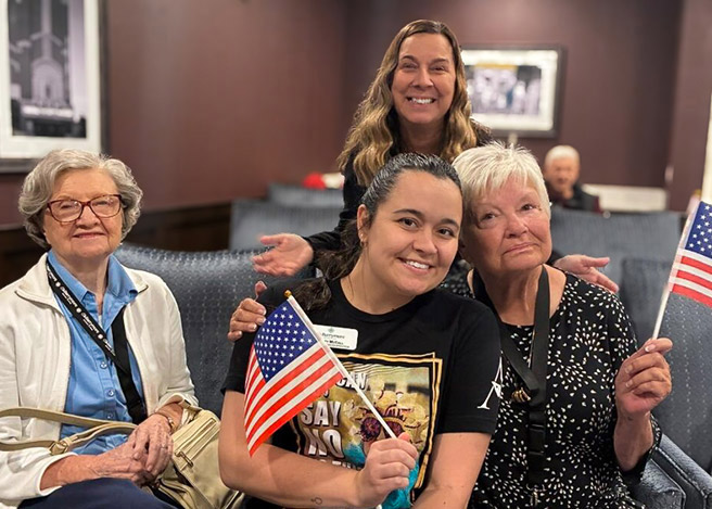 Team members and senior friends smile together, holding patriotic flags during an event.