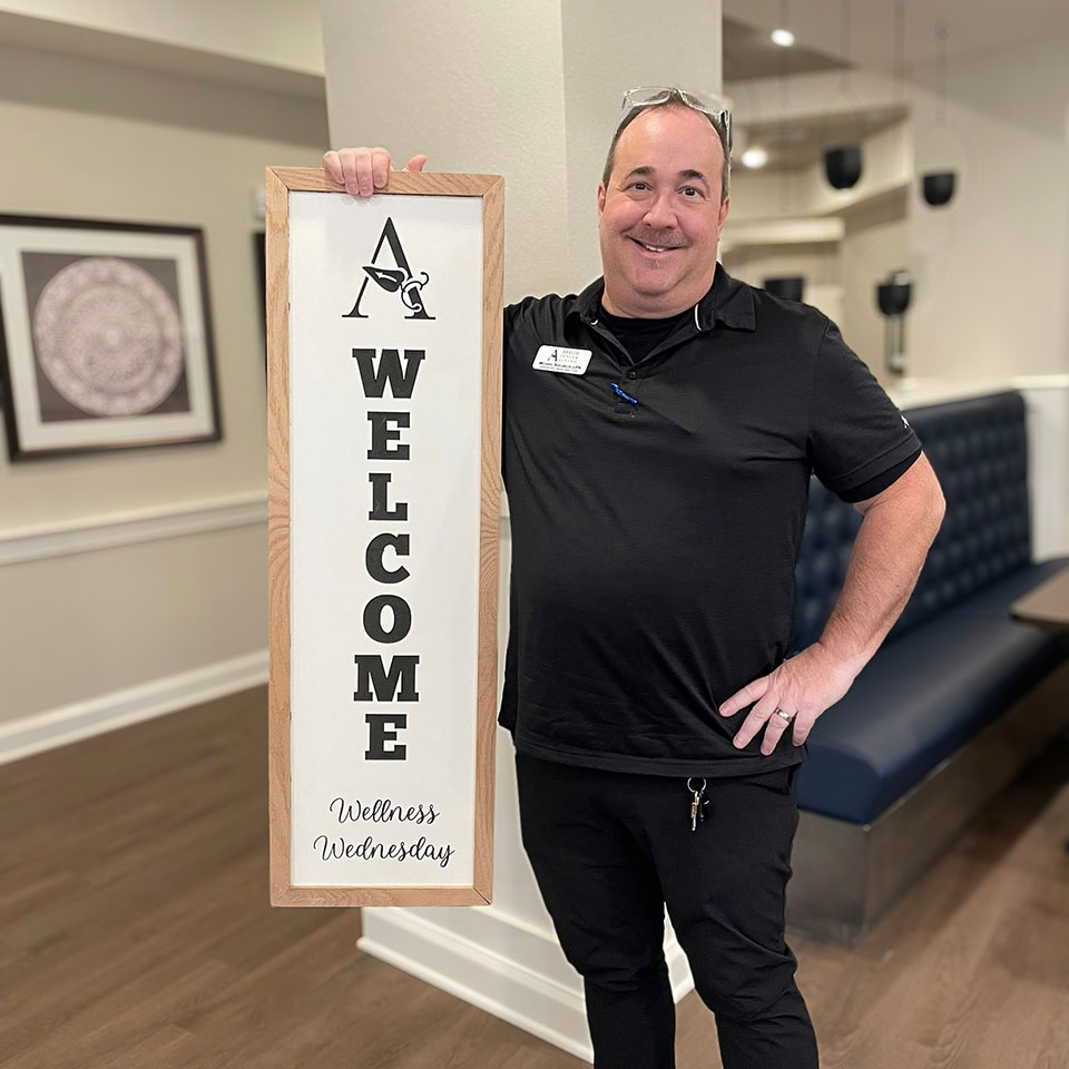 A team member smiles, posing with an Arrow Welcome sign for Wellness Wednesday.