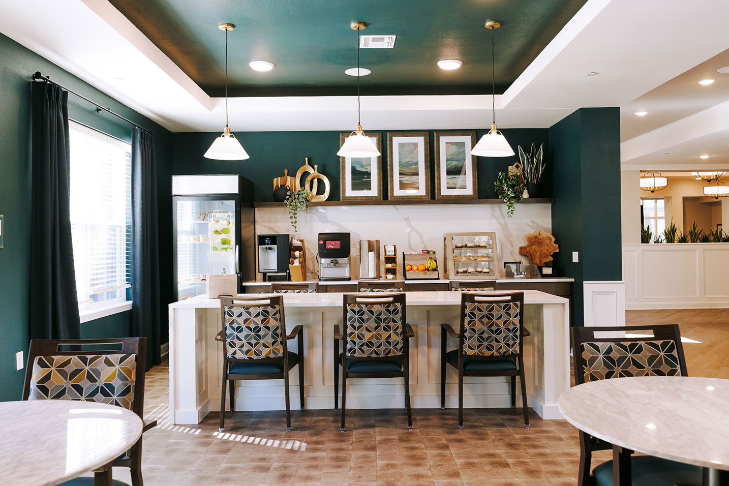 A bistro area at Barrymore Senior Living, showcasing deep green and white with earth tone accents, grab and go food options, and elegant lighting.