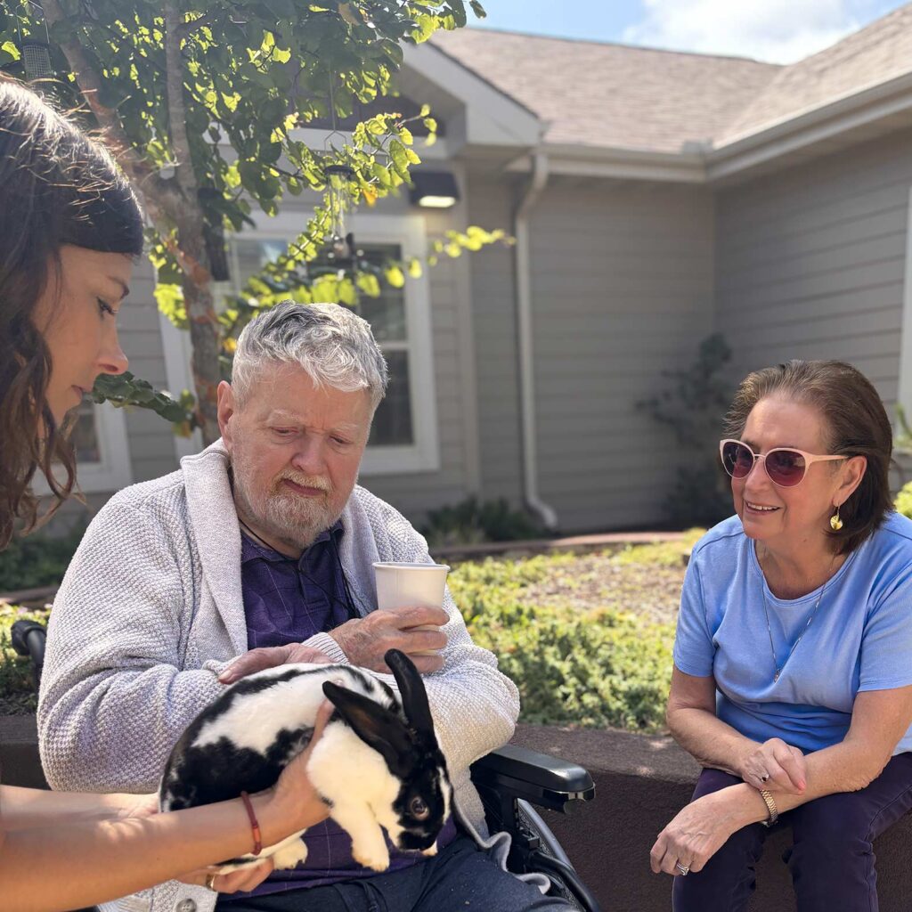 A man and woman look on in interest while a younger woman holds out a black and white rabbit.