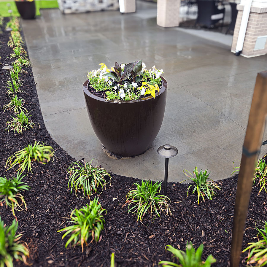 A planter filled with flowers rests beside a freshly planted flower bed.